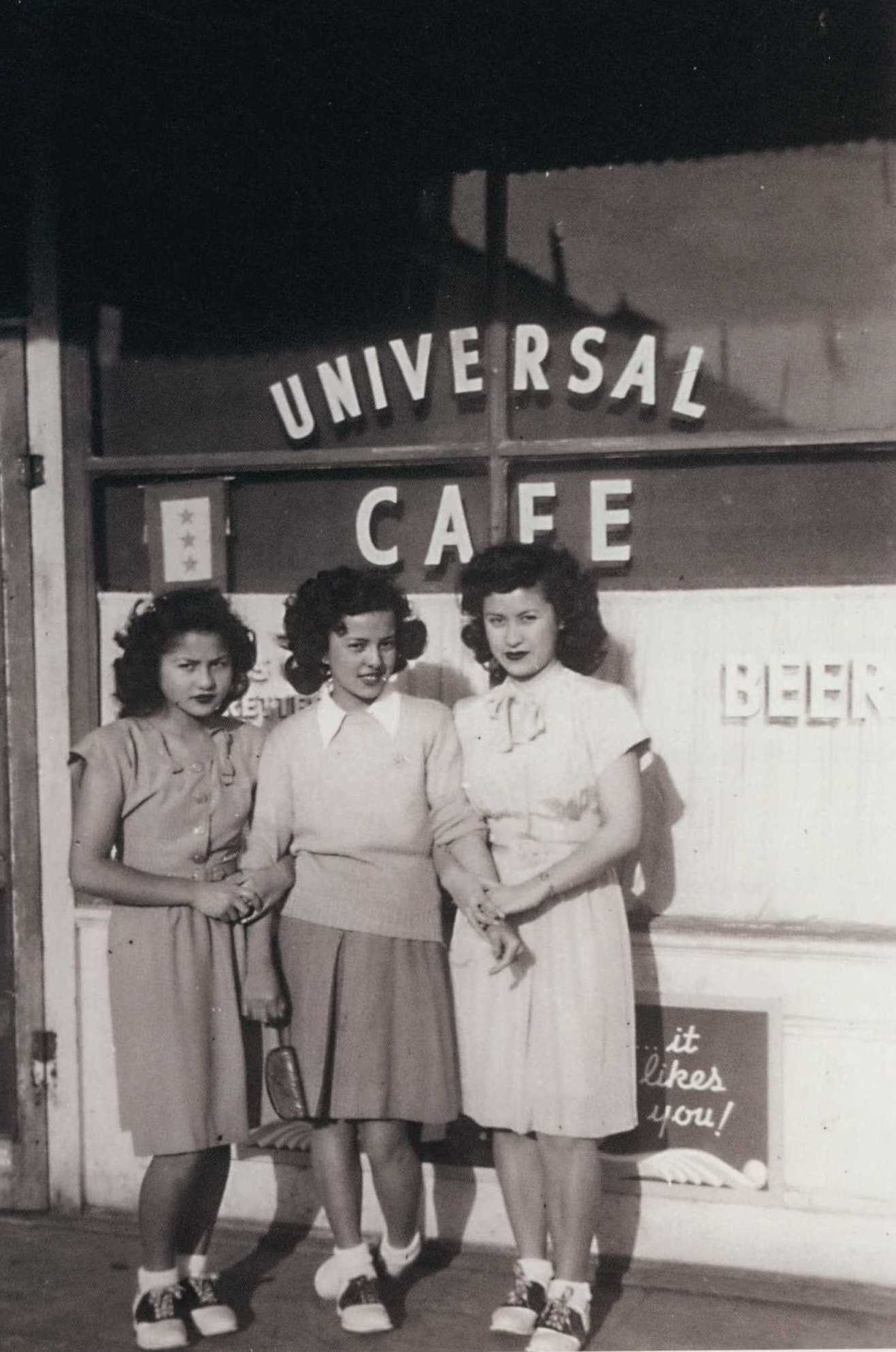 Three young women stand in front of a store called the "Universal Cafe."