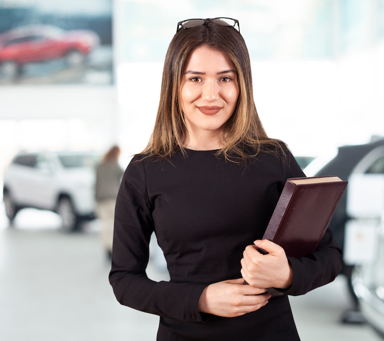 woman with notebook standing near row of cars