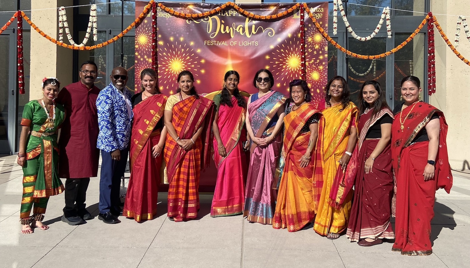employees in colorful outfits pose in front of diwali banner